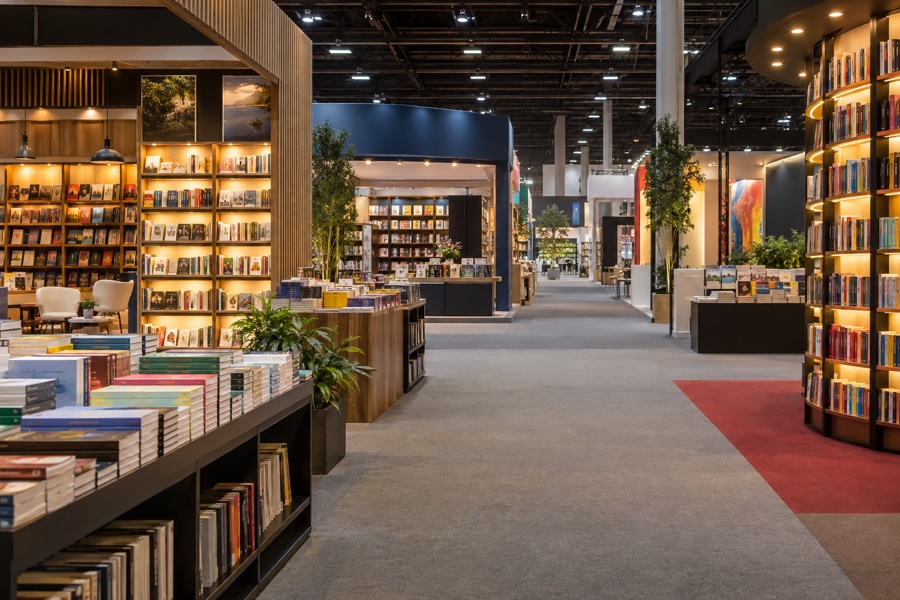 Pavilhão de feira do livro com estantes e mesas de lançamentos