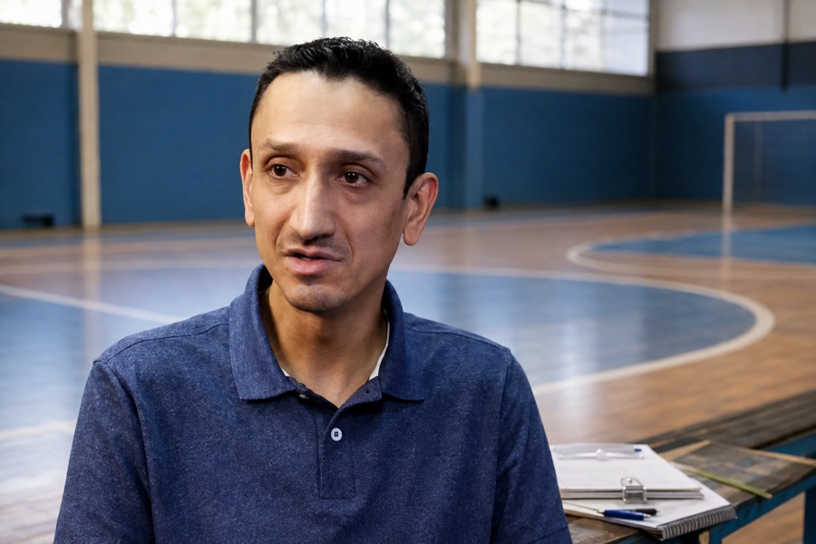 Piero Trentim em ginásio escolar com prancheta de atividades pedagógicas