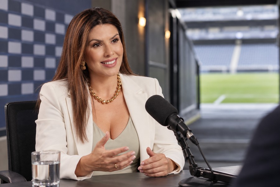 Carina Batista em entrevista diante de uma área de imprensa esportiva