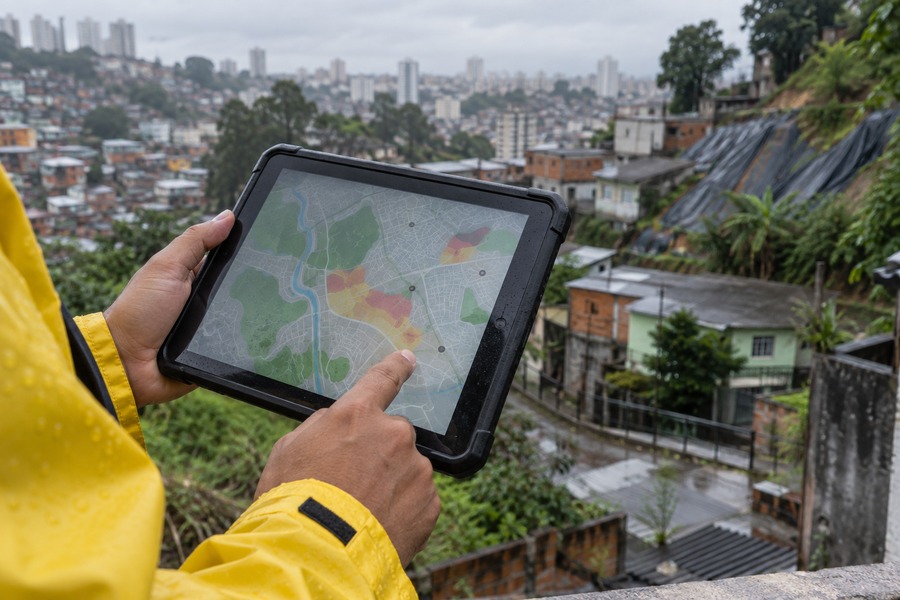 Agente com tablet e mapa em área urbana de encosta sob chuva